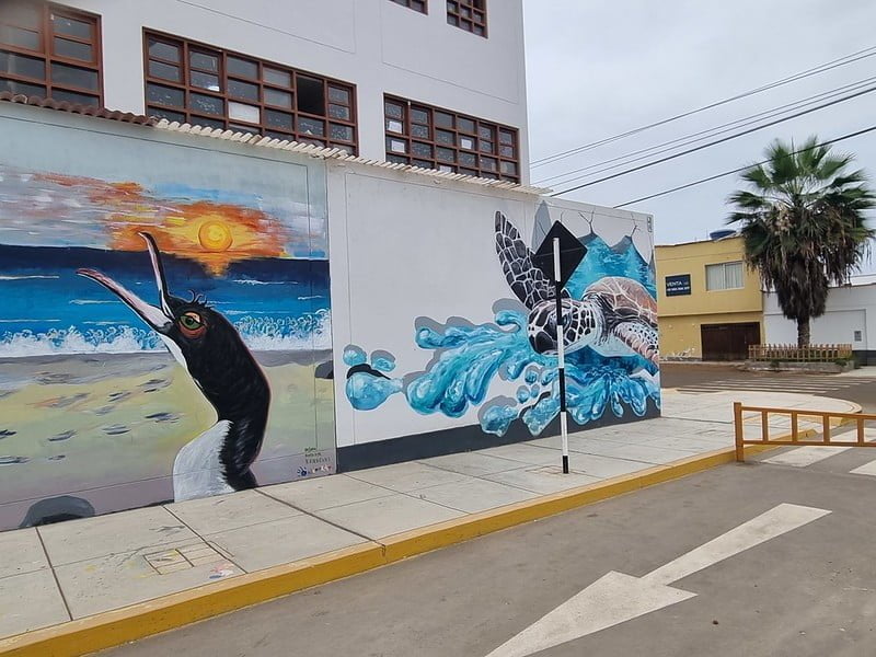 Mural of a bird in front of a sunset and of a turtle breaking through a white wall. 