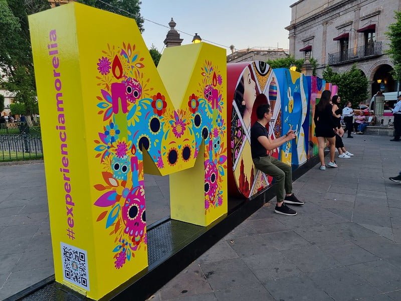 3D colourful, free-standing sign in the centre of Morelia, Mexico with some people standing in front of it. 